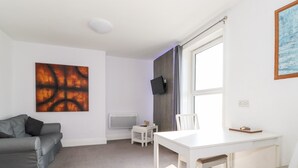 Una sala moderna con un sofá gris, una mesa de comedor blanca y un televisor montado en la pared.
