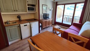 A compact kitchen with a microwave, sink, and dishwasher, a dining area with a wooden table and chairs, and a television in the corner. - Cozy south-facing apartment, 4 people, near funicular (Isola 2000)