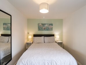 A neatly arranged bedroom with a large bed, two bedside tables with lamps, a mirror, and floral artwork on the wall.