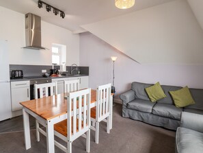 A compact kitchen with a dining table and chairs, a grey sofa with green cushions, and a modern light fixture.