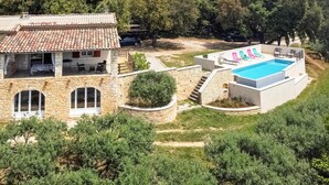 A two-story stone house with a swimming pool, outdoor seating, and a garden.