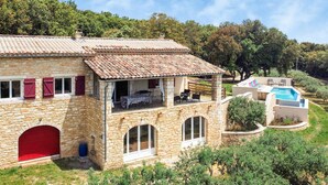 A stone house with a tiled roof, a red door, and a swimming pool.