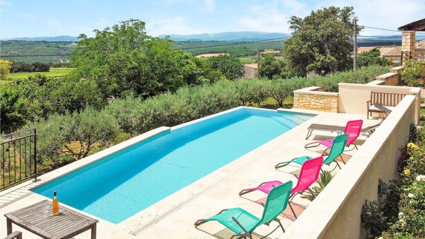 A rectangular swimming pool with a clear blue water, surrounded by a stone wall. There are several colorful lounge chairs aligned along the pool's edge.