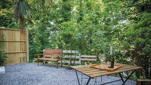 An outdoor seating area with a wooden table, benches, and a bottle of wine. - Croft Court - 1 Bedroom Apartment - Tenby (Tenby)