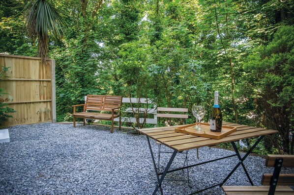 An outdoor seating area with a wooden table, benches, and a bottle of wine. - Croft Court - 1 Bedroom Apartment - Tenby (Tenby)