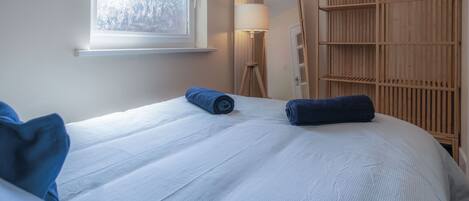 A bedroom with a large bed, a wooden wardrobe, a floor lamp, and a window with frosted glass.