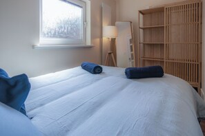 A bedroom with a large bed, a wooden wardrobe, a floor lamp, and a window with frosted glass. - Croft Court - 1 Bedroom Apartment - Tenby (Tenby)