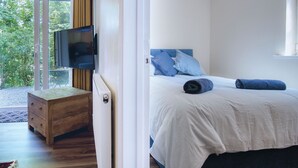 A bedroom with a bed, a TV, and a wooden nightstand. - Croft Court - 1 Bedroom Apartment - Tenby (Tenby)