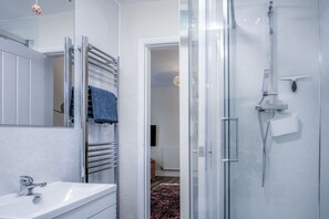 A modern bathroom with a glass shower enclosure, a white sink, and a towel rack with a blue towel. - Croft Court - 1 Bedroom Apartment - Tenby (Tenby)