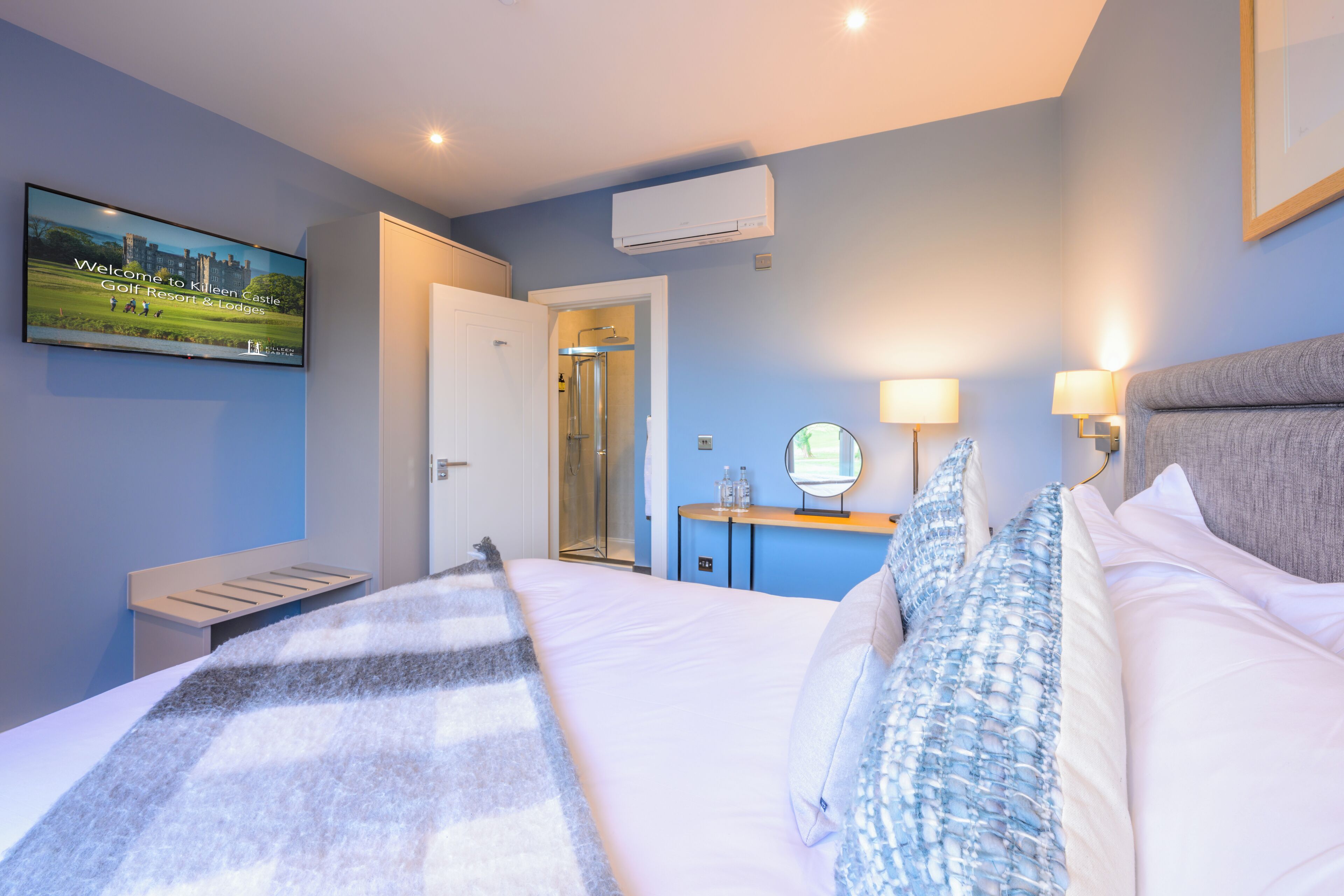 Una habitación de hotel con cama, mesitas de noche, televisor, espejo y aire acondicionado.