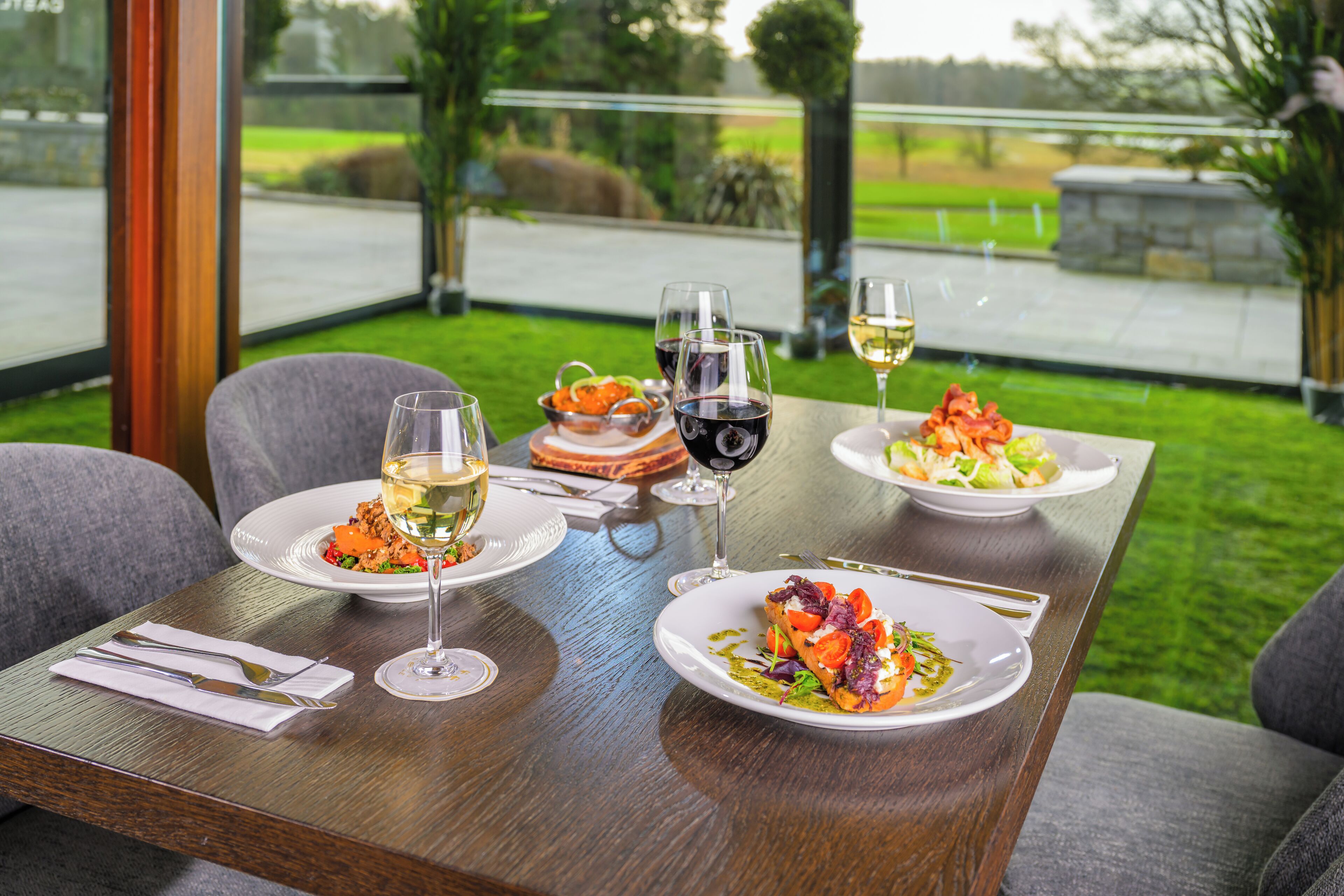 Een eettafel met borden eten en wijnkaraffen, in een ruimte met uitzicht op een groen landschap.
