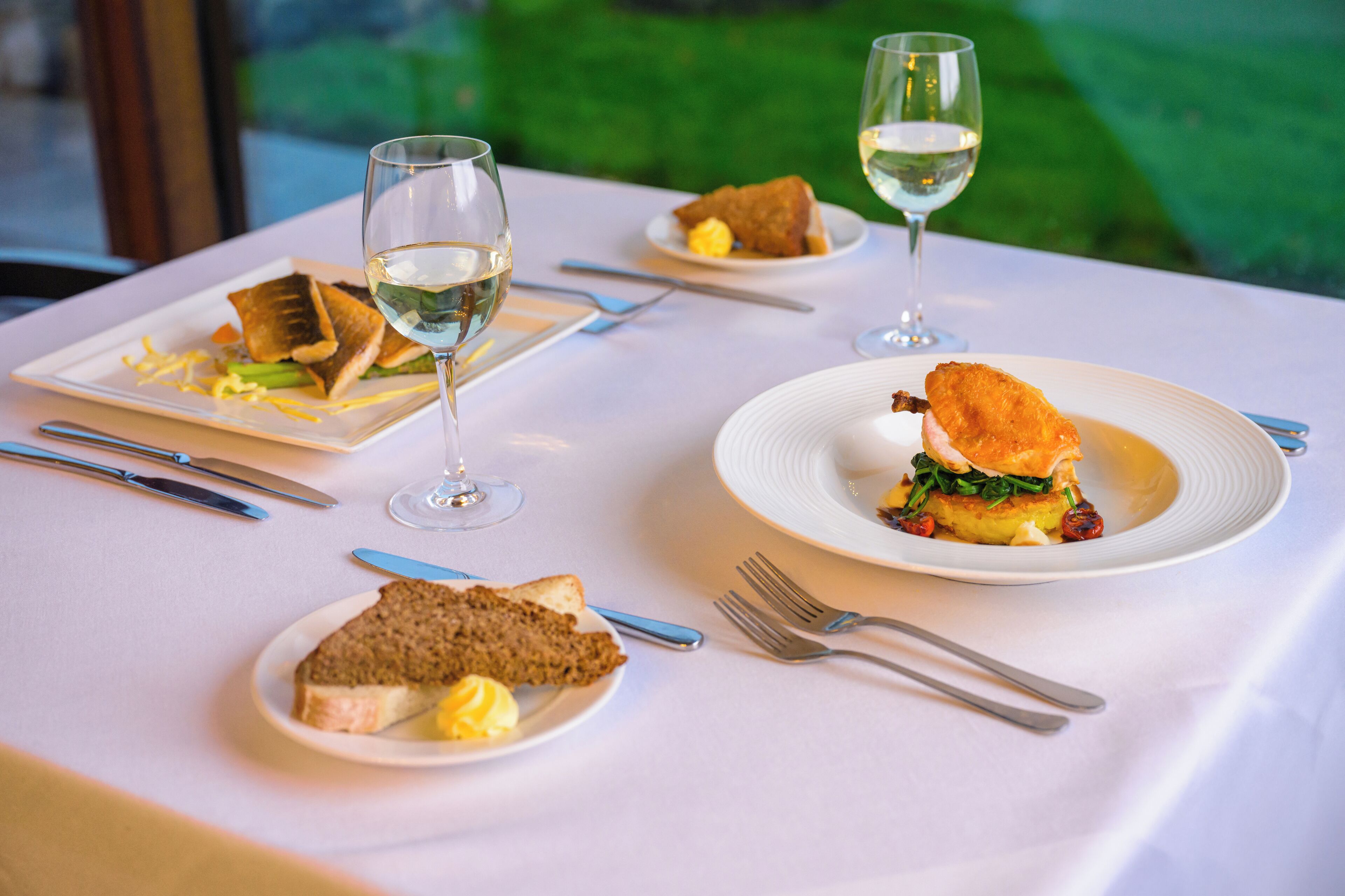 A table set with plates of food, glasses of white wine, and cutlery.