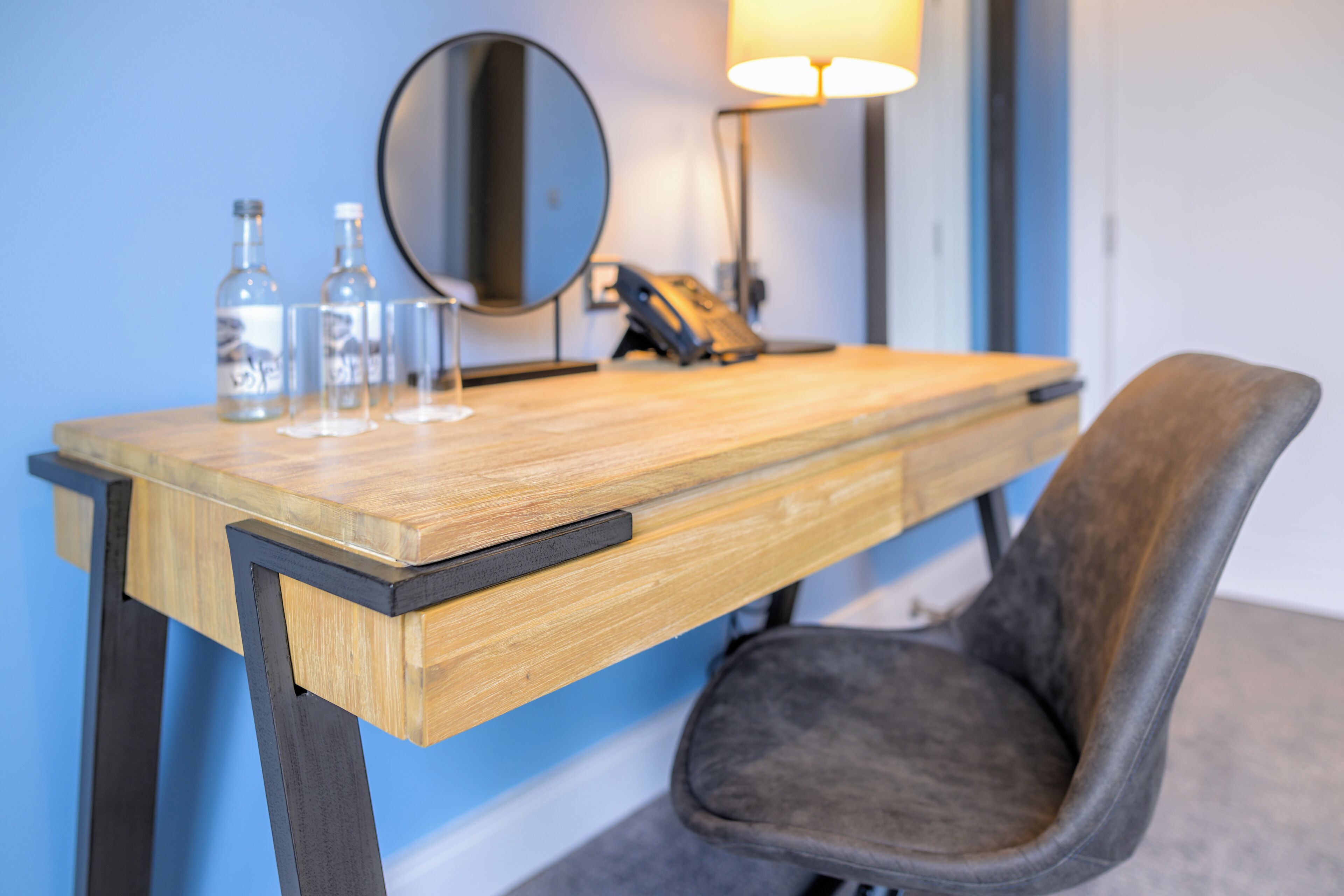 A wooden desk with a mirror, two bottles, and a lamp.
