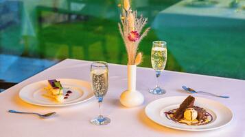 A table with three plates of dessert, two glasses of champagne, and a vase with dried flowers.