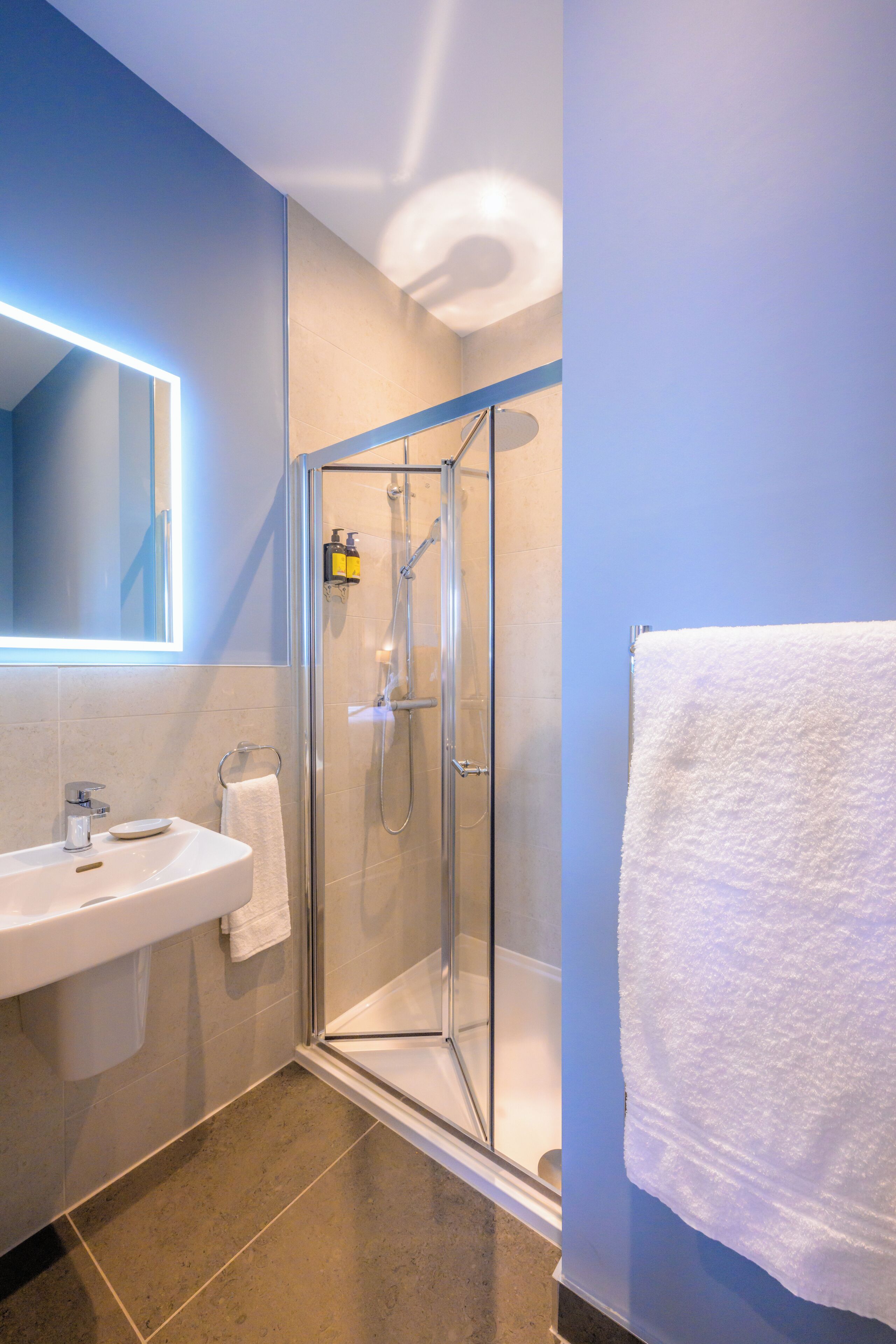 Un baño moderno con ducha de vidrio, lavamanos blanco y espejo con luz integrada.