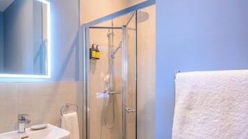 Un baño moderno con ducha de vidrio, lavamanos blanco y espejo con luz integrada.