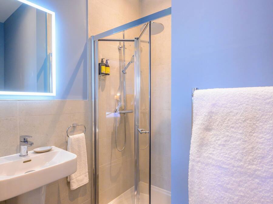 Un baño moderno con ducha de vidrio, lavamanos blanco y espejo con luz integrada.