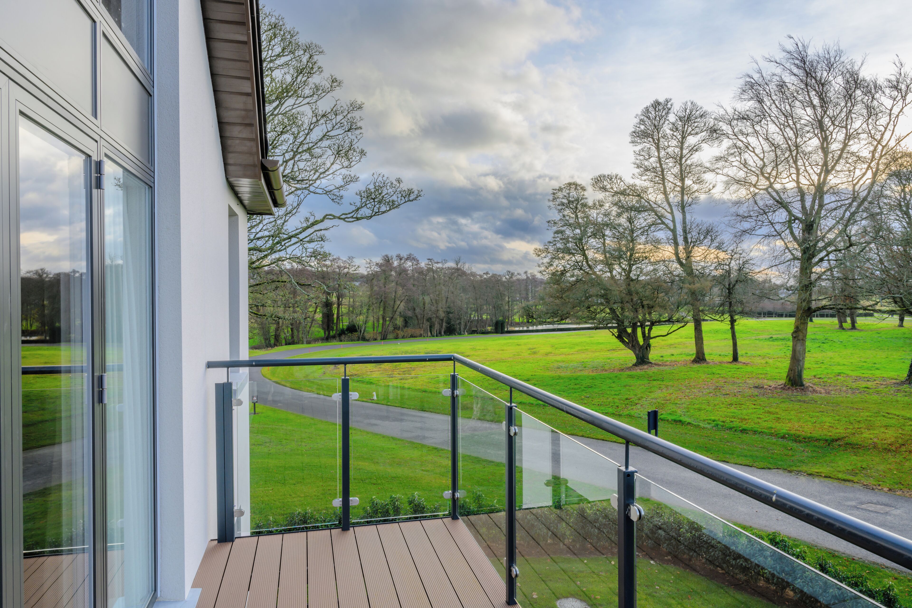 Un bâtiment moderne doté de grandes fenêtres et d’un balcon donnant sur un paysage verdoyant, avec des arbres et une route.