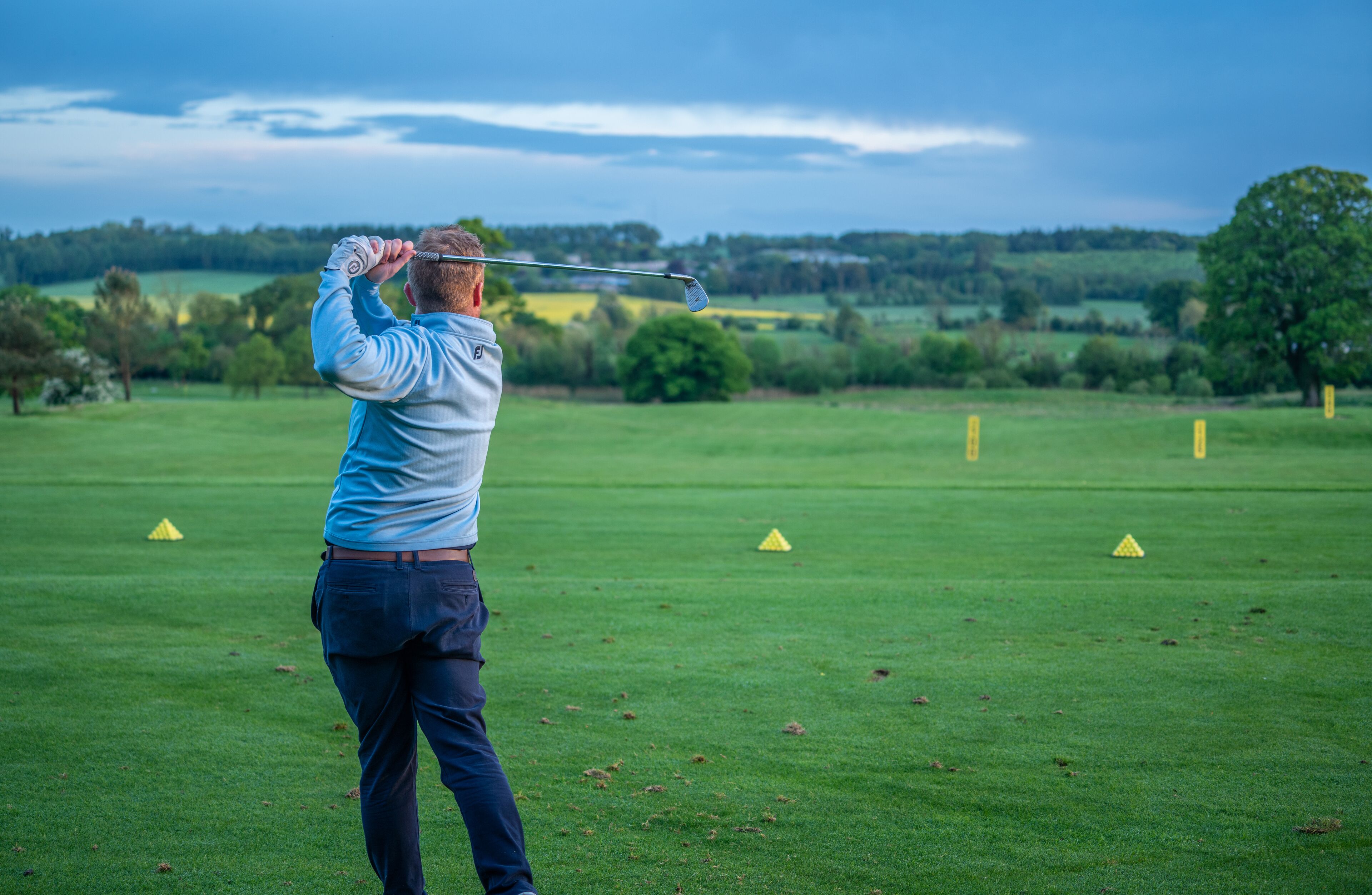 A person playing golf on a course with green grass and trees in the background.