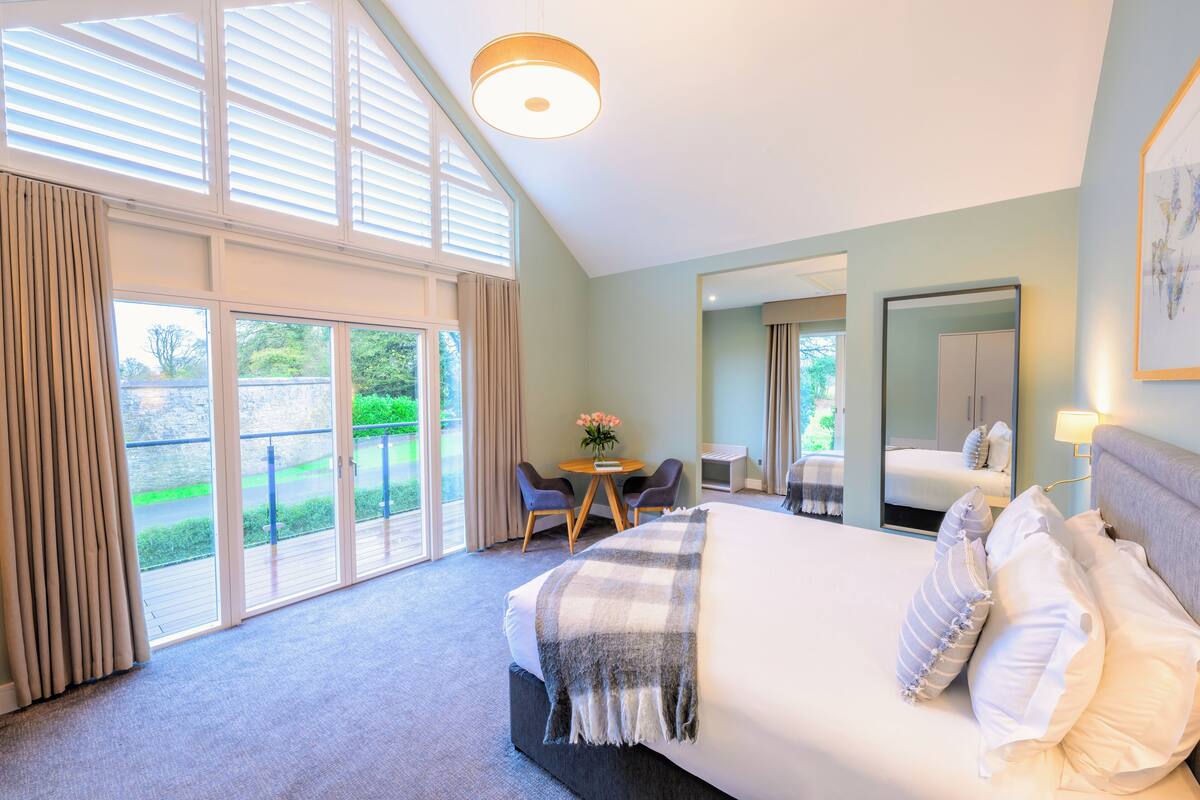 A hotel room with a large bed, a round table, and a balcony with curtains.