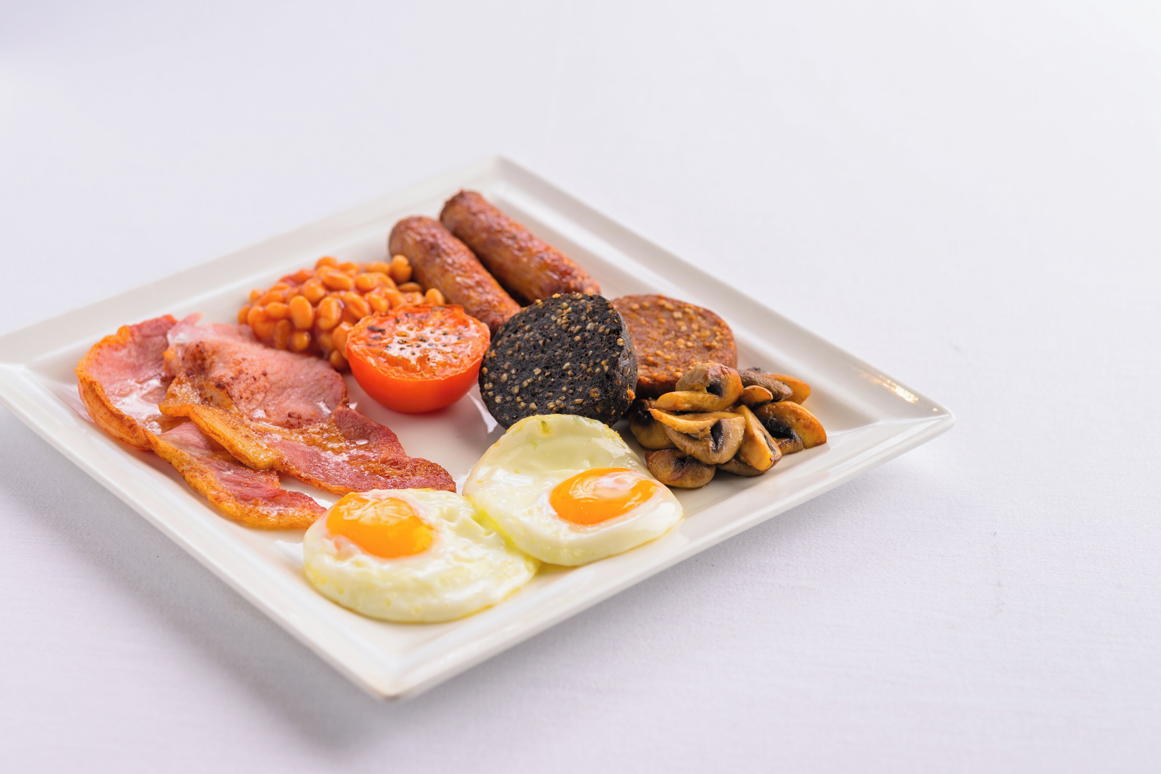 A breakfast plate with bacon, eggs, sausages, beans, mushrooms, and a tomato.