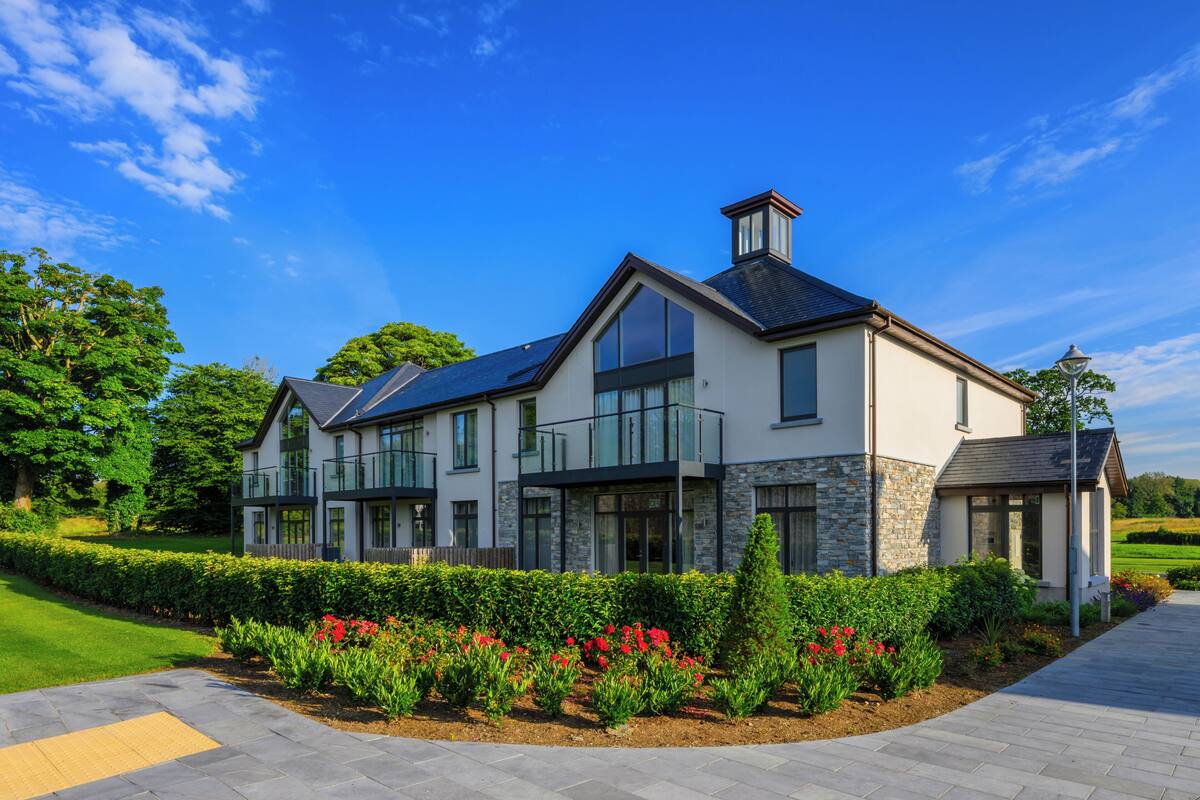 A modern two-story house with a stone facade, large windows, and a landscaped garden with red flowers.
