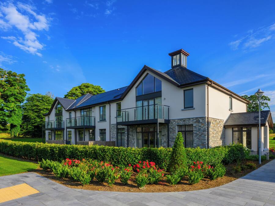 A modern two-story house with a stone facade, large windows, and a landscaped garden with red flowers.