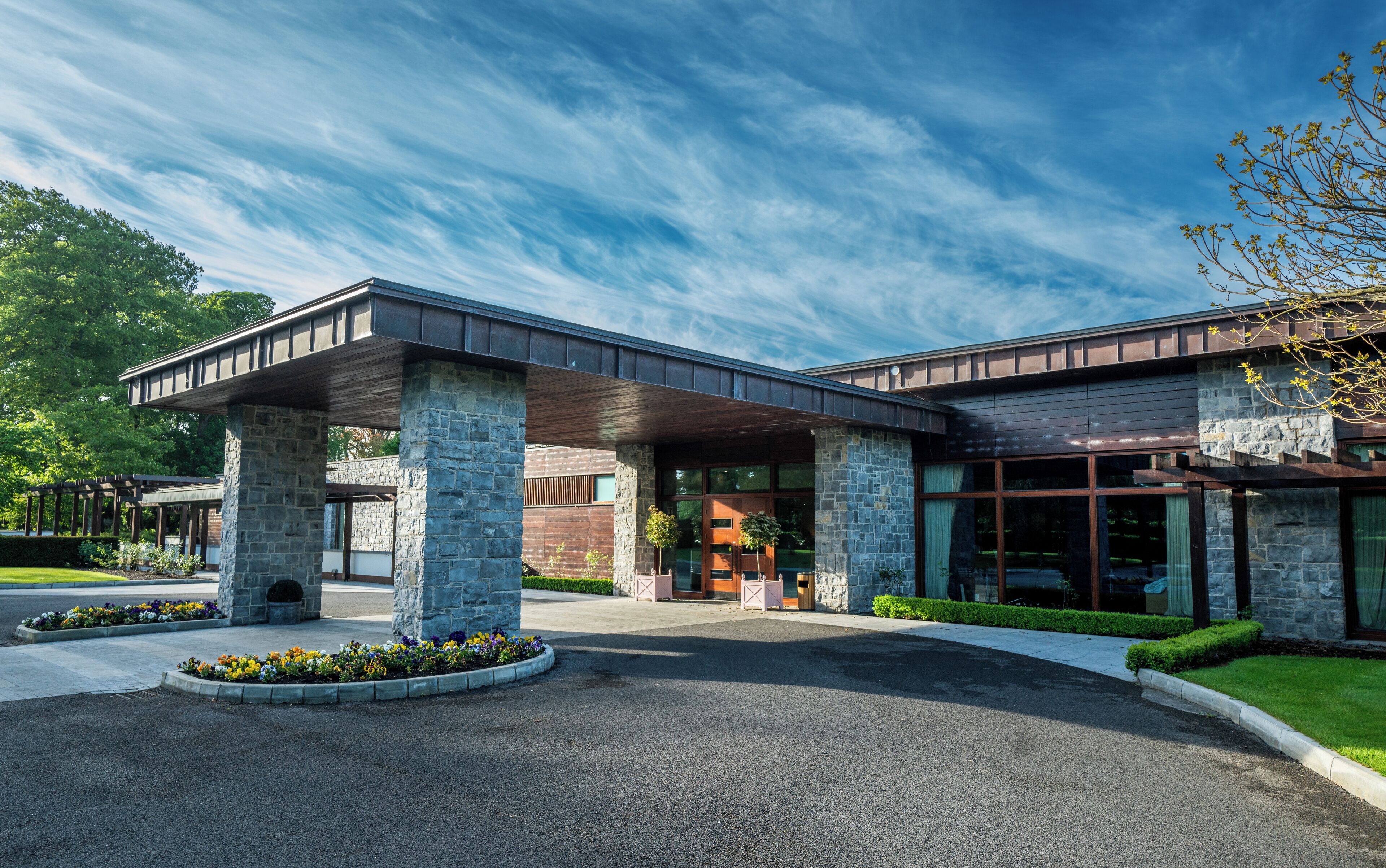 A modern building with a stone facade, large windows, and a covered entrance area.