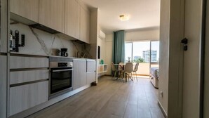 Een moderne keuken met inbouwapparatuur, een eethoek met een tafel en stoelen, en uitzicht op de stad door grote ramen.
