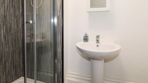 Une salle de bain avec une douche à parois de verre, un lavabo blanc et un miroir au-dessus du lavabo.