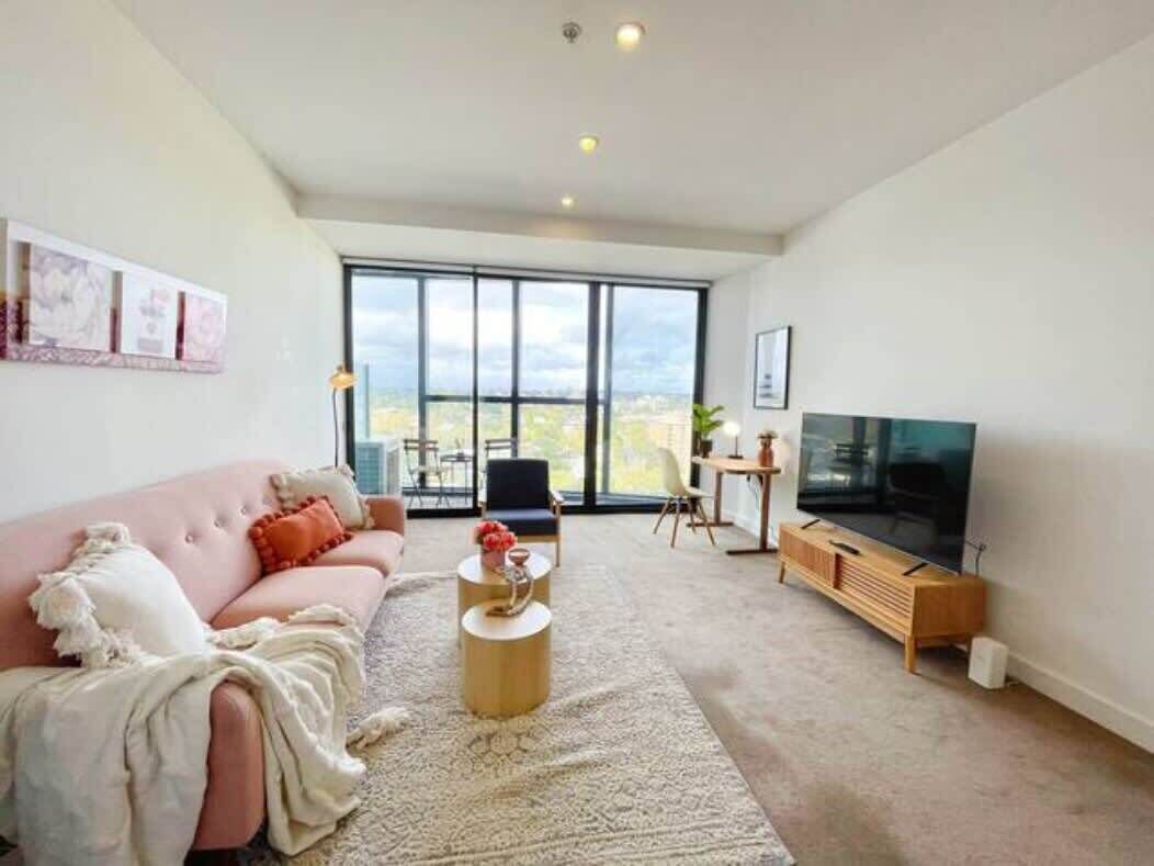 A modern living room with a large window, a pink sofa, a coffee table, and a TV.