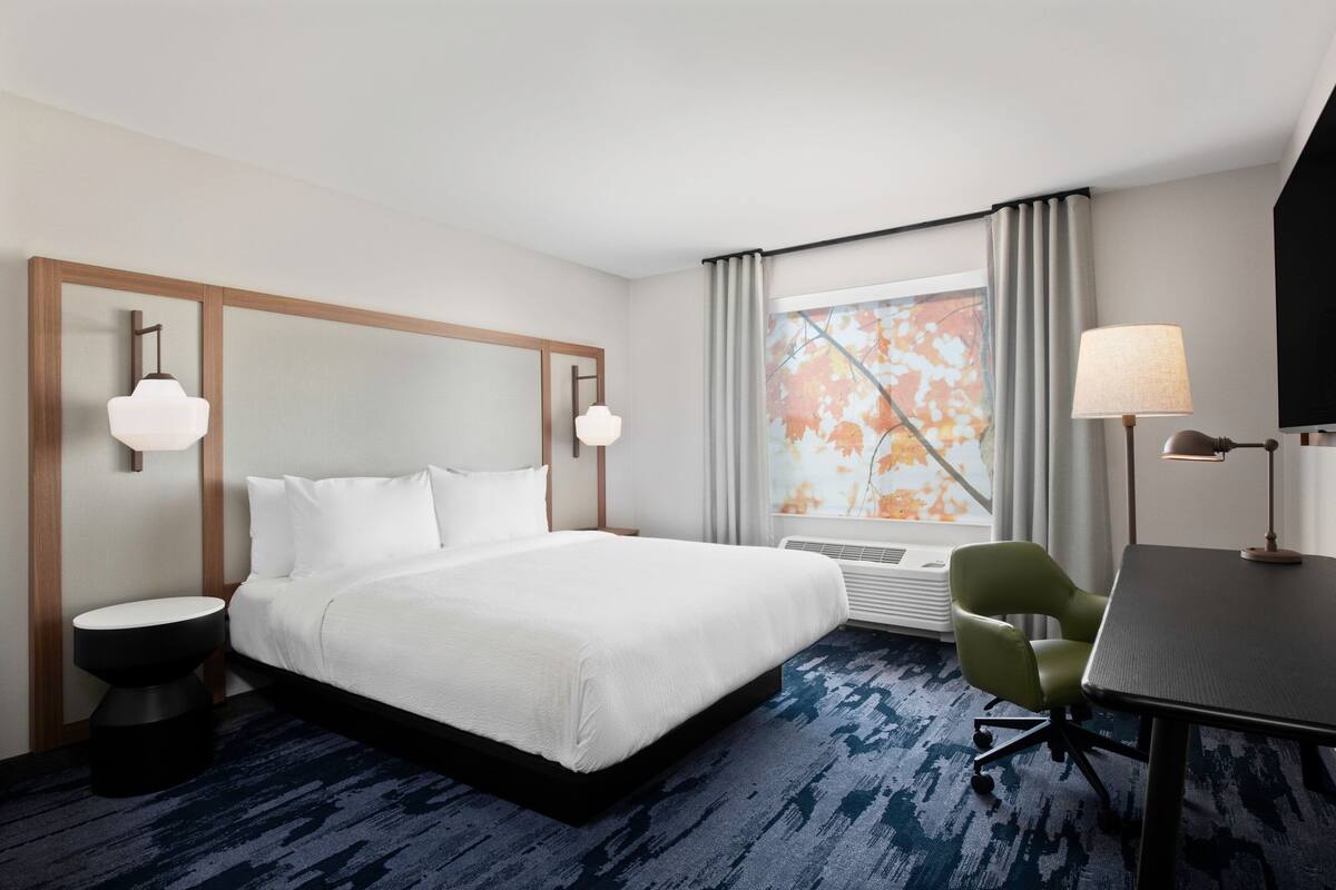 A hotel room with a large bed, a desk, a chair, a TV, and a window with curtains.