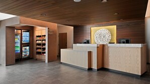 A modern reception area with a wooden reception desk, a vending machine, and a refrigerated display. - Fairfield Inn by Marriott & Suites Chino (Chino)