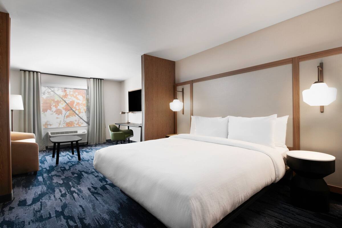 A hotel room with a large bed, a desk with a chair, a small table, and a TV.