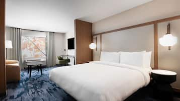 Una habitación de hotel con una cama grande, un escritorio con silla, una mesita y un televisor.