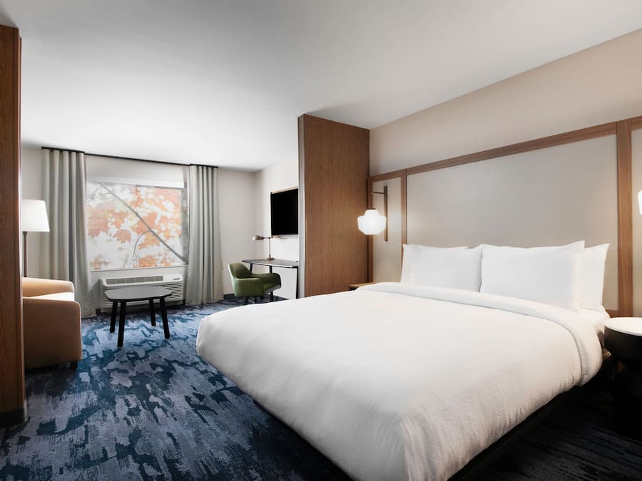 Una habitación de hotel con una cama grande, un escritorio con silla, una mesita y un televisor.