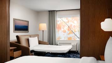 A hotel room with a bed, a desk, a chair, a lamp, a window with curtains, and a painting on the wall.