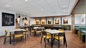 A modern restaurant with multiple dining tables and booths, a large black sign on the wall, and a view of the ocean through large windows. - Fairfield Inn by Marriott & Suites Chino (Chino)