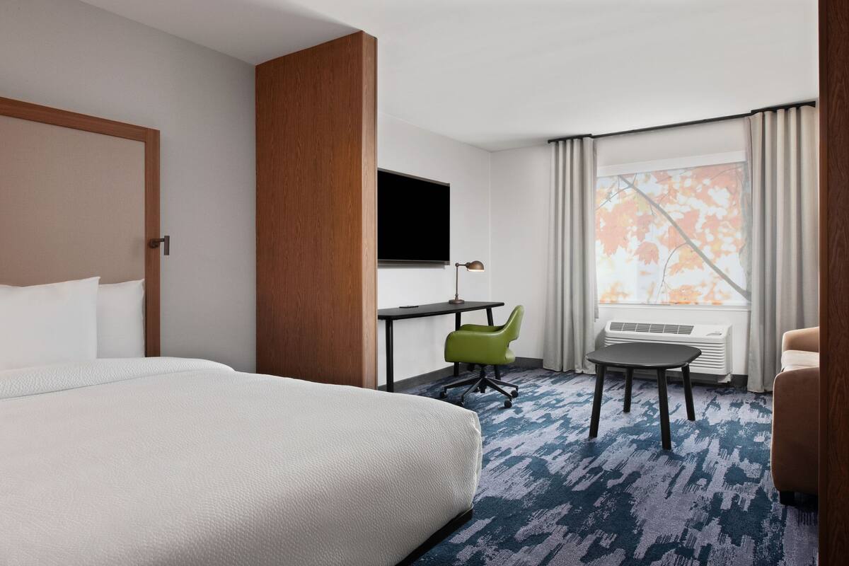 A hotel room with a large bed, a desk with a chair, a TV, and a window with curtains.