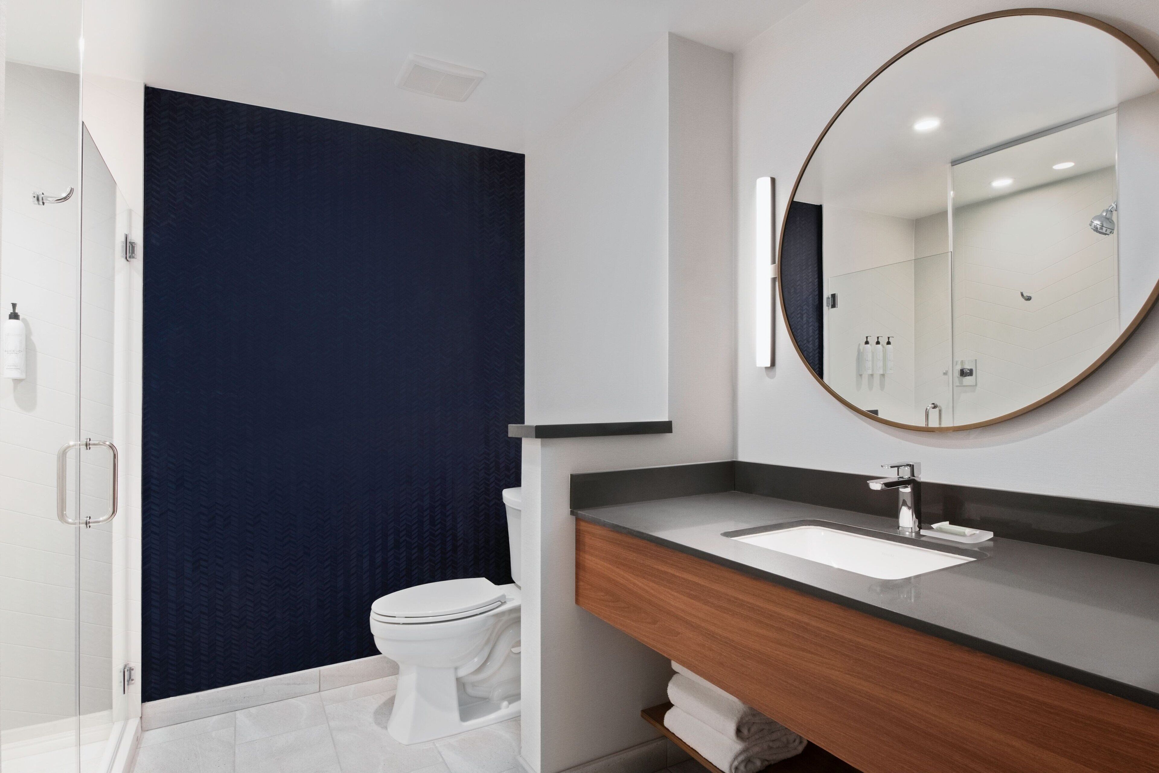 A modern bathroom with a white toilet, a dark blue shower curtain, a wooden vanity with a white sink, and a large mirror.