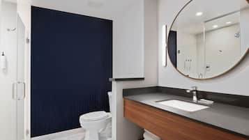 A modern bathroom with a white toilet, a dark blue shower curtain, a wooden vanity with a white sink, and a large mirror.