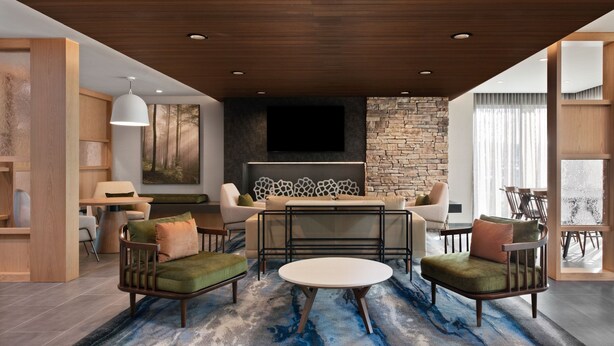 A modern living room with a stone fireplace, a flat-screen TV, and a round coffee table. - Fairfield Inn by Marriott & Suites Chino (Chino)