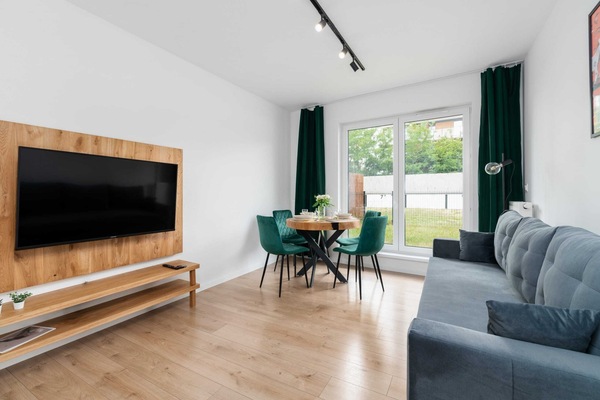 A bright and cozy living room featuring a modern TV unit, a comfortable sofa, and large windows letting in ample natural light.