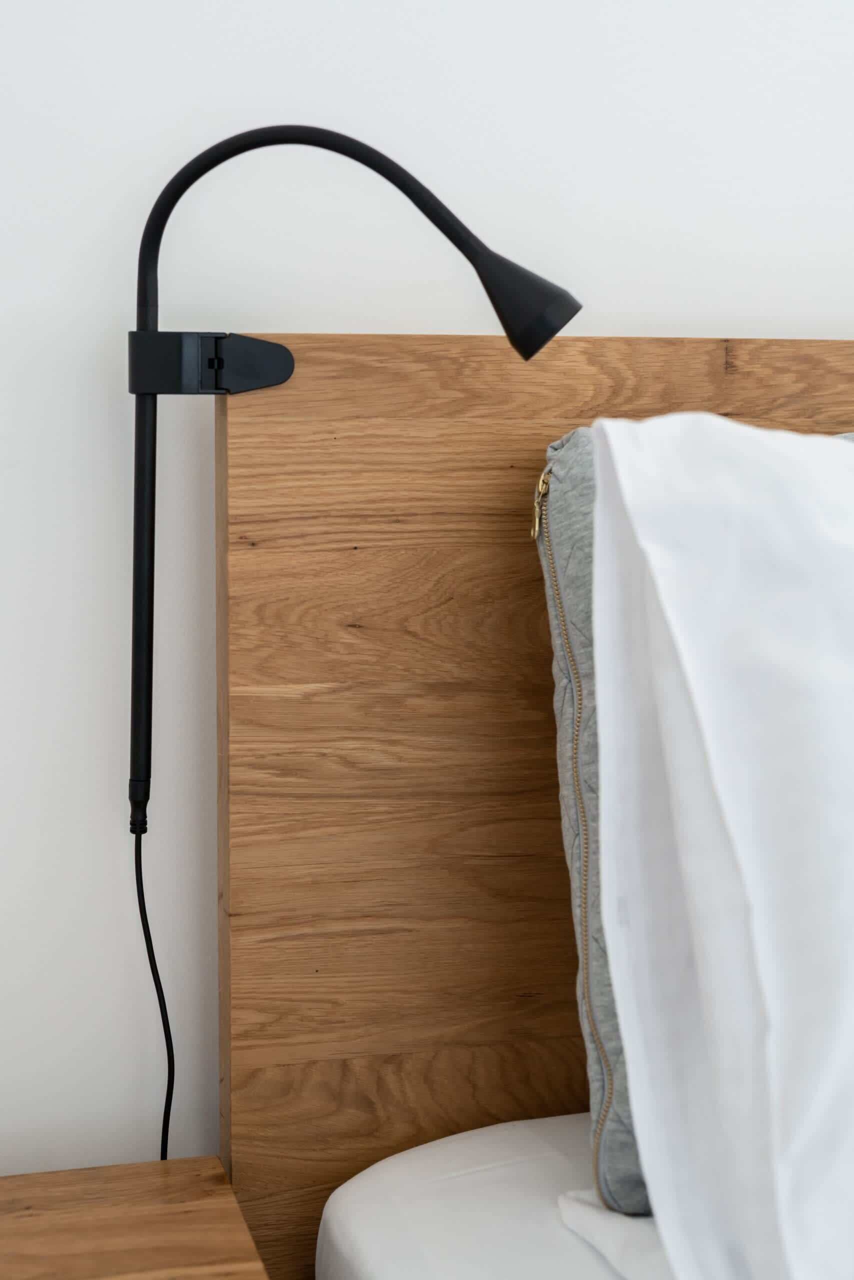 A modern bed with a wooden headboard, a black adjustable lamp, and a white blanket.