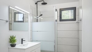 A modern bathroom with a glass shower enclosure, a white sink with a plant, and a large mirror.