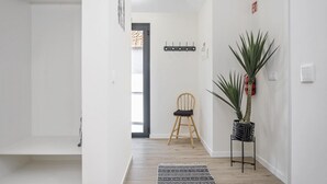 A hallway with a wooden floor, a black and white patterned rug, a wooden chair, and a potted plant.