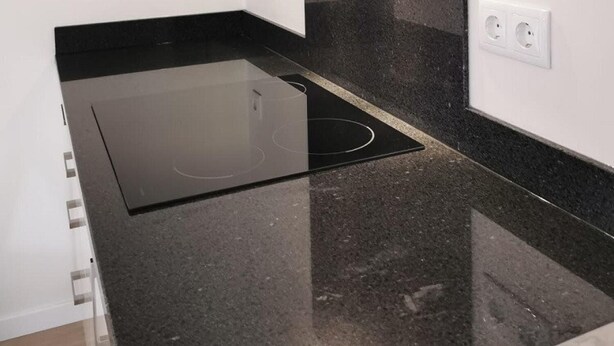 A modern kitchen with a black countertop, a built-in stove, and a sleek backsplash.
