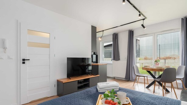 Een moderne hotelkamer met een bed, een televisie, een zithoek met een tafel en stoelen, en een balkon met uitzicht.