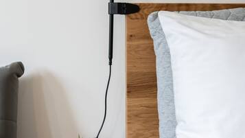 Ein Bett mit Holz-Kopfstück, ein Nachttisch mit Topfpflanze und eine schwarze Schreibtischlampe.