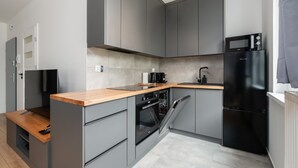 Een kleine keuken met grijze kastjes, een houten aanrechtblad, een inbouwoven, een zwarte koelkast en een magnetron.